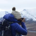 Photographer capturing a mountain landscape, wearing a blue jacket and wool hat.