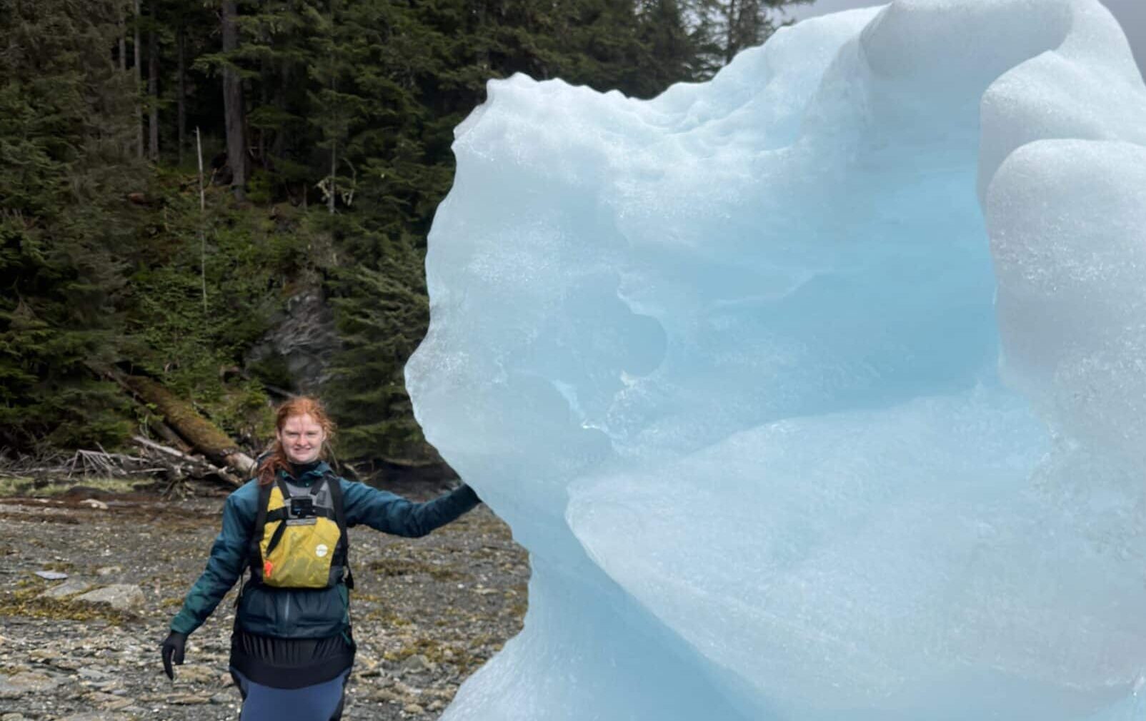 Ella and a large piece of glacier ice ashore on a beach in remote Alaska