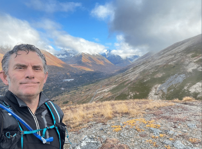 Tour guide James stands in a mountain pass with some fall colors on the ground cover