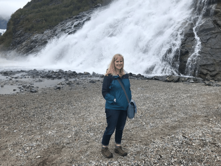 Elizabeth is a Salmon Berry Tours local guide who shares Alaska with visitors from around the world. She is pictured here at Nugget Falls in Juneau at the Mendenhall Glacier.